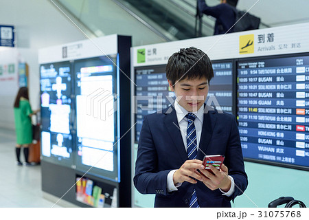 空港内の到着ロビーでスマホを見るビジネスマン 31075768
