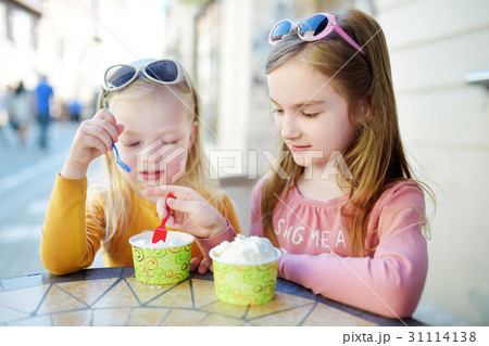 Two little sisters eat ice cream in outdoor cafe Two little sisters eat ice cream in outdoor cafe 31114138