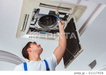 Worker repairing ceiling air conditioning unit 31117458