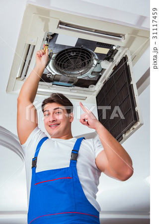 Worker repairing ceiling air conditioning unit 31117459