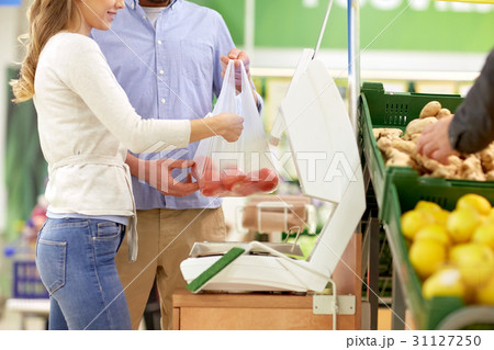 happy couple weighing tomatoes on scale at grocery 31127250