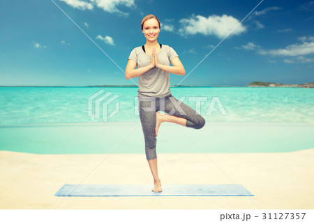 woman making yoga in tree pose on beach 31127357