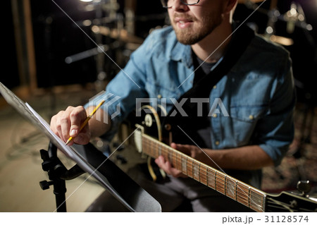 man with guitar writing to music book at studio 31128574
