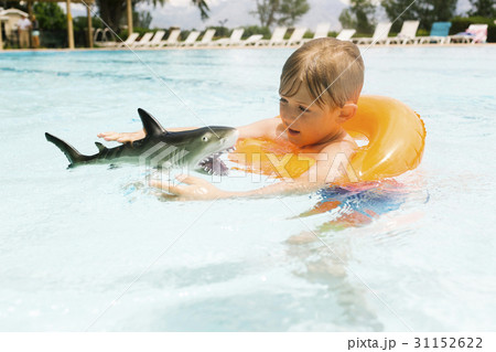 Boy (6-7) playing with toy shark in swimming pool Boy (6-7) playing with toy shark in swimming pool 31152622
