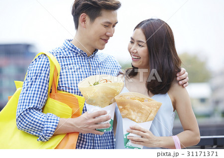 a man with an arm on his girlfriend's shoulder and crepes on hands. 31171371