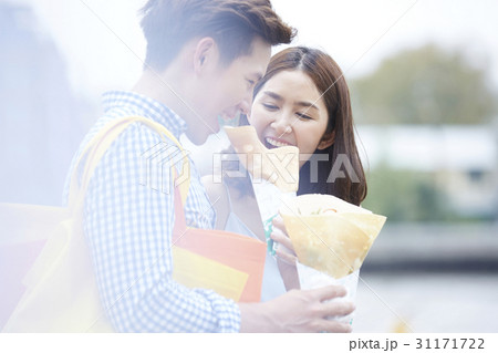 A couple is smiling and eatting two crepes outdoors. A couple is smiling and eatting two crepes outdoors. 31171722
