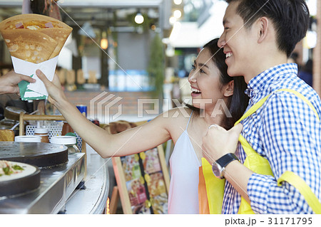 A couple is smiling and taking one crepe from someone. 31171795