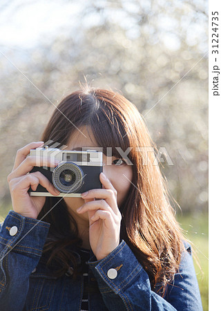 カメラ女子 カメラ 一眼レフ レトロ 女性 代 桜 目線 花 ロング 長髪 かわいい の写真素材