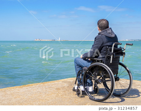 Disabled young man sitting in a wheelchair and looks at the sea 31234857
