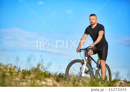 Young man cycling on a green meadow against blue Young man cycling on a green meadow against blue 31273345