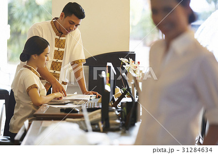 a receptionist is pointing at the booking notes for his colleague. 31284634