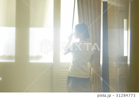 Maid is pulling up curtains in a room. 31284773