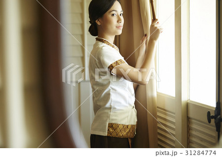 Housekeeper is opening curtains of the window in the room. 31284774