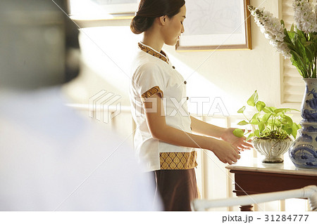 Female staff is looking and touching plant vase on the table. 31284777