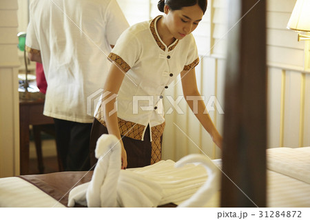 A staff is preparing bed in hotel room. 31284872