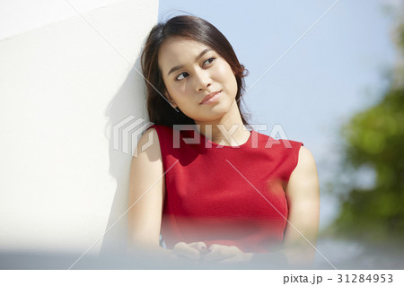 A woman in a red dress is leaning against the wall and looking. A woman in a red dress is leaning against the wall and looking. 31284953