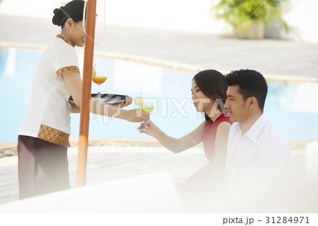 A couple is receiving cocktails from a waitress near a pool. A couple is receiving cocktails from a waitress near a pool. 31284971
