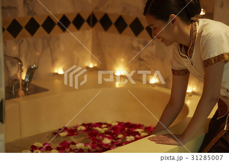 A housekeeper is preparing a bathtub with flowers in a hotel room. 31285007
