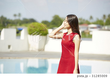 A woman in a red dress is touching her hair and smiling with closed eyes. A woman in a red dress is touching her hair and smiling with closed eyes. 31285009