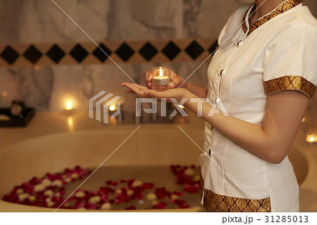 A staff is holding a candle in a bathroom with bathtub, flowers, candles. A staff is holding a candle in a bathroom with bathtub, flowers, candles. 31285013