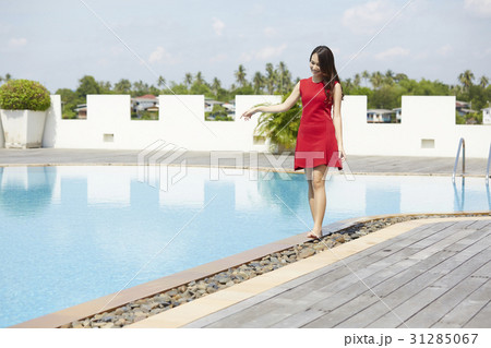 The woman in red dress is walking barefoot around the pool 31285067