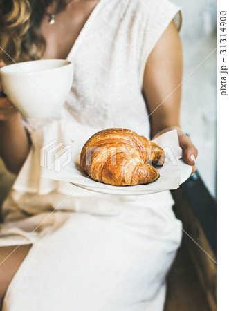 Young blond woman holding fresh croissant and cup Young blond woman holding fresh croissant and cup 31314900