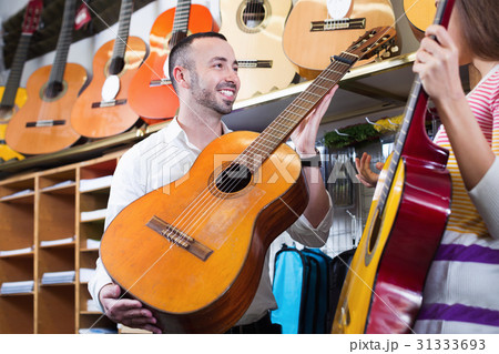 Friendly shopgirl helping male client to select guitar 31333693