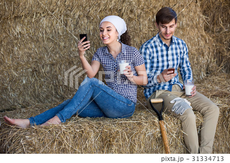 portrait of two farmers taking a pause in the hay and having their phones in hands 31334713