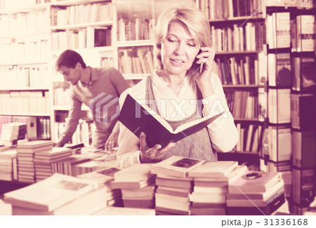 Smiling mature woman customer looking at book Smiling mature woman customer looking at book 31336168