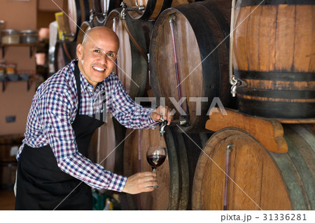 Smiling mature man seller filling wine from wood 31336281