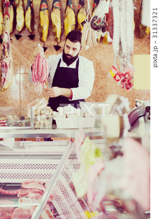 Adult man seller showing different sausages Adult man seller showing different sausages 31337321