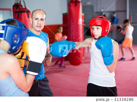 Boxing instructor closely follows the teenagers in sparring 31338286