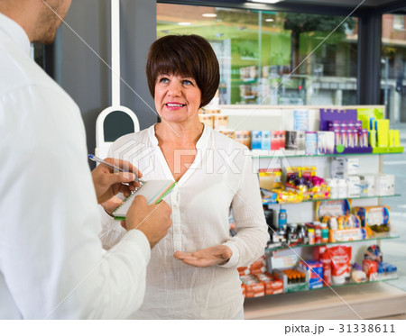 Smiling man pharmacist wearing uniform assisting customers Smiling man pharmacist wearing uniform assisting customers 31338611