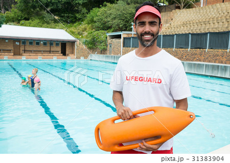 Lifeguard standing with rescue buoy near poolside 31383904