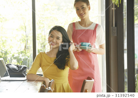 a photo of a waitress holding a cup, standing behind a smiling woman a photo of a waitress holding a cup, standing behind a smiling woman 31392540