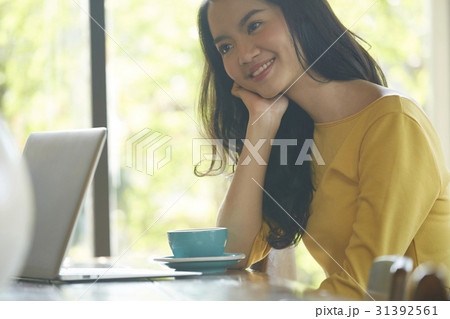 a woman is sitting and smiling beside a cup of coffee, laptop. 31392561