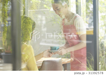 A waitress is giving a coffee to customer, view through the window. A waitress is giving a coffee to customer, view through the window. 31392578