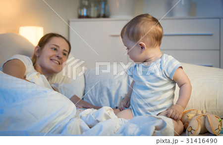 Baby sitting on bed at night and looking at mother 31416490