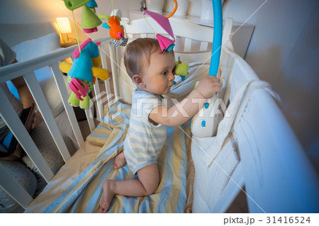 Baby standing in crib and playing with toy 31416524