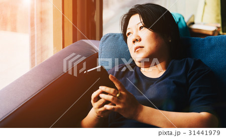 Asia women 40s holding smartphone thinking on sofa 31441979