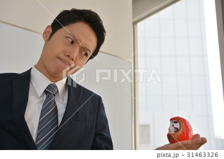 頑張るぞ！だるまを手のひらに載せて、にらめっこする若いビジネスマン、ガッツ、やる気、気合 31463326