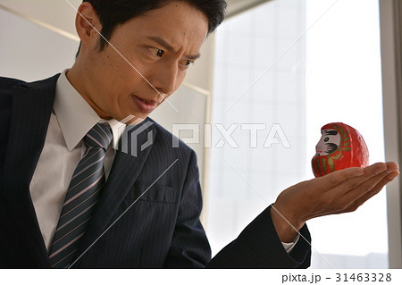 だるまを手のひらに載せて、にらめっこする若いビジネスマン、ガッツ、やる気、気合 31463328