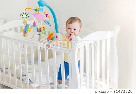baby boy crying and holding to the side of crib 31473520