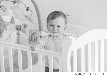 portrait of baby standing in crib and crying 31473521