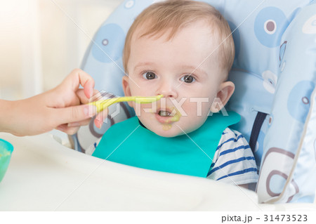 baby in apron eating fruit sauce from spoon 31473523