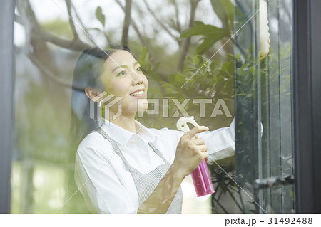 a happy lady is spraying and cleaning glass window 31492488