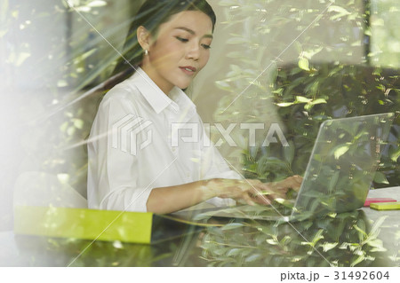 a woman sitting behind the glass is working on laptop. 31492604