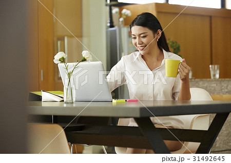 a happy woman holding a mug is looking the laptop. 31492645