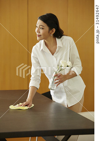 a maid is cleaning a table, holding a vase and looking at something. 31492647