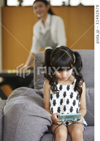 a little girl is sitting and playing handheld video game. 31492678